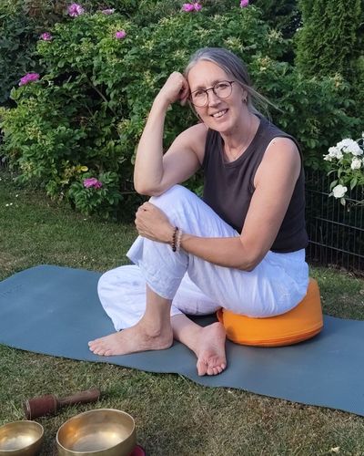 Heike sitzt auf einer Yogamatte im Garten, daneben zwei Klangschalen