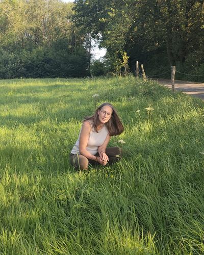 Heike kniet im hohen Gras und betrachtet blühende Wildkräuter am Wegesrand